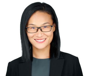 professor wearing a black blazer and gray shirt in front of a white backdrop